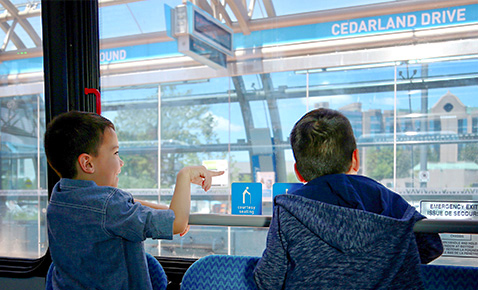 Two young boys looking out the window of a bus as they pass cedarland station.
